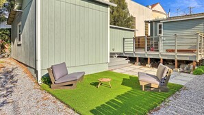 Un espace patio aménagé avec deux chaises et une petite table, entouré d’une pelouse artificielle verte.