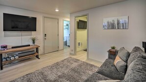 Un salon moderne avec un téléviseur à écran plat, un canapé gris, un meuble de rangement en bois avec des haltères, et un tapis gris.