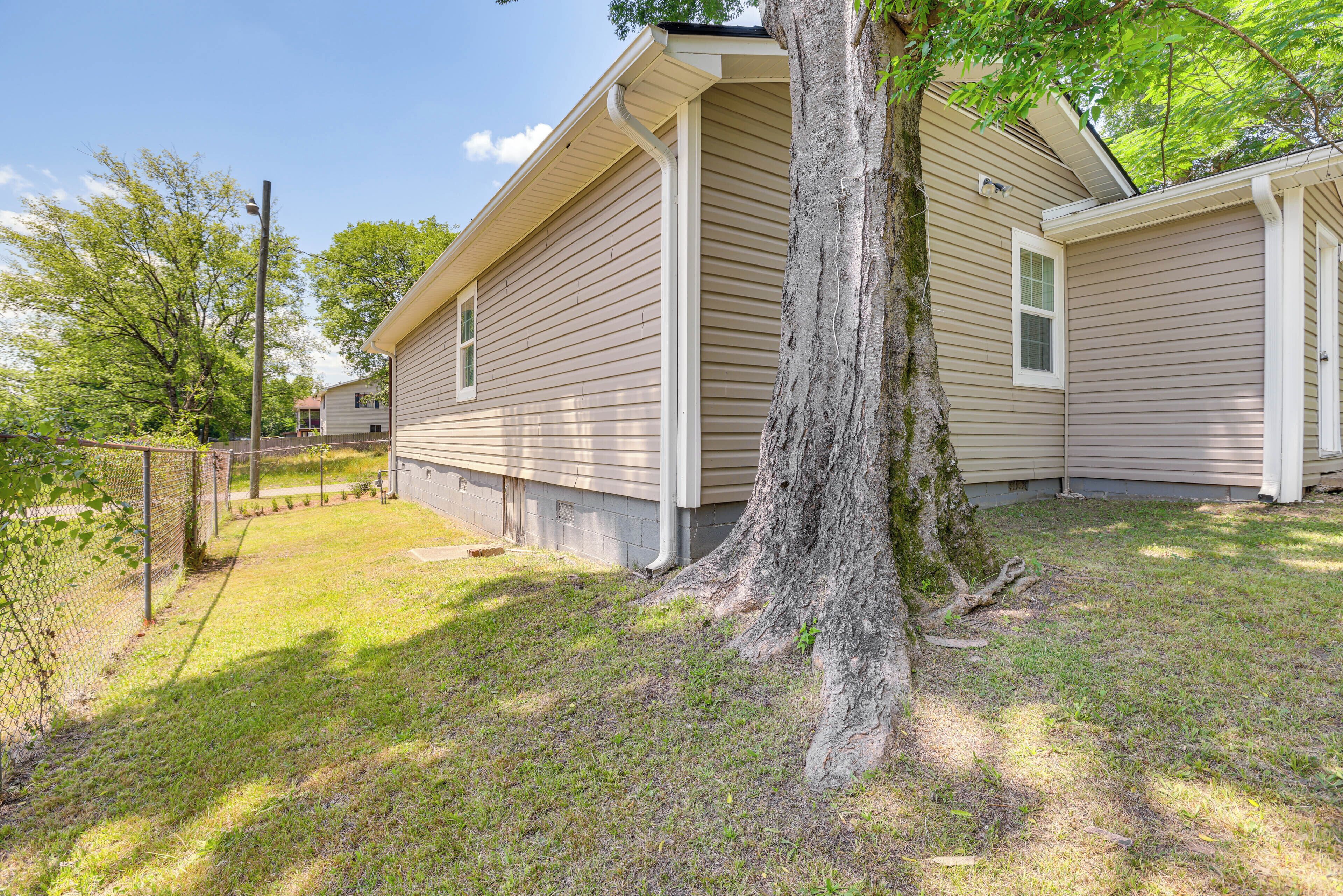 A single-story house with a front yard, a tree, and a chain-link fence.