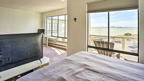 Quarto de hotel com cama, televisão e uma grande janela com vista para um rio e para a paisagem urbana.
