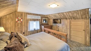 A bedroom with a bed, wooden walls, a welcome sign, a television, and a door. - Illinois Vacation Rental Home: Pets Welcome (Palestine)