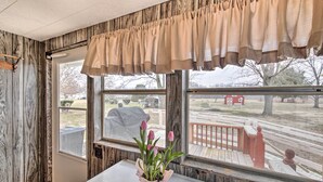 A room with a wooden wall, a window with a view of a deck and outdoor area, and a potted plant with flowers on a table. - Illinois Vacation Rental Home: Pets Welcome (Palestine)
