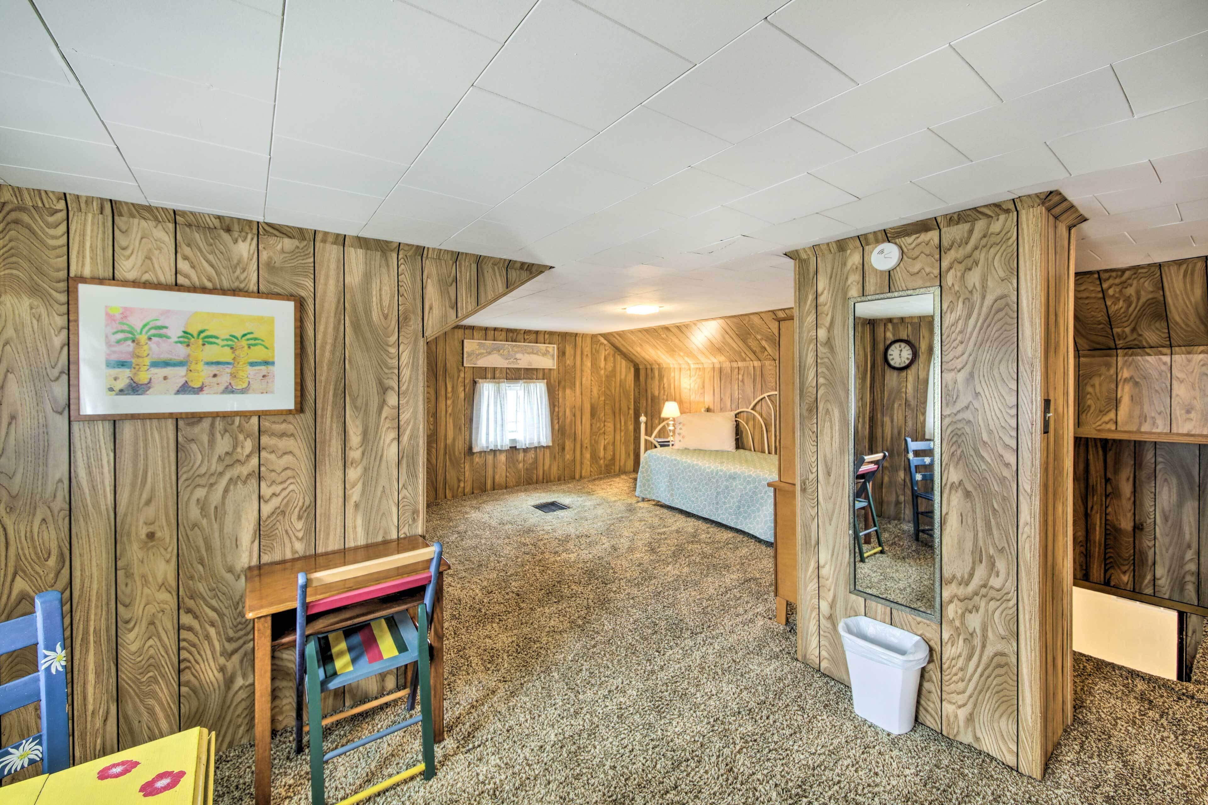 A room with wooden panel walls, a bed, a desk with a chair, a mirror, and a framed picture on the wall.
