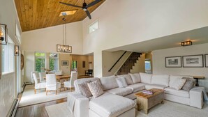 Un salón espacioso con un amplio sofá modular, una mesa de centro de madera y una escalera que lleva a un nivel superior.