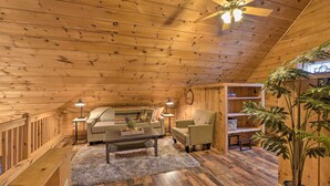 A cozy wooden cabin interior with a sofa, armchair, and a ceiling fan.