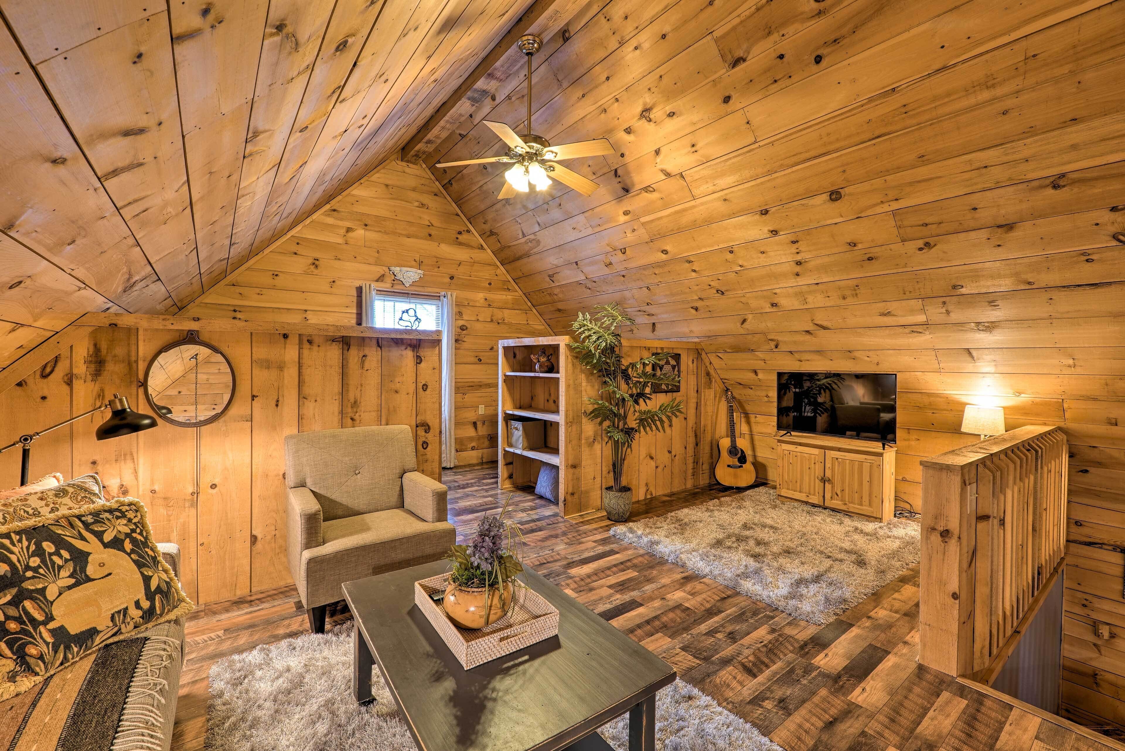 A cozy, wooden-paneled attic room with a ceiling fan, a sofa, a coffee table, a TV, and a guitar.