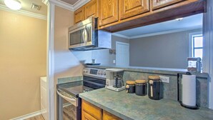 A kitchen with wooden cabinets, a stainless steel microwave, a coffee maker, and a paper towel holder.