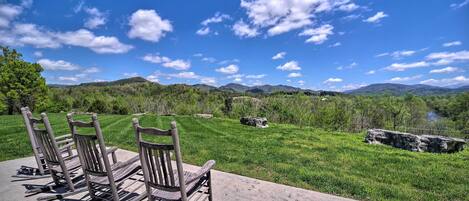 A patio with wooden rocking chairs overlooking a grassy landscape with mountains in the distance.
