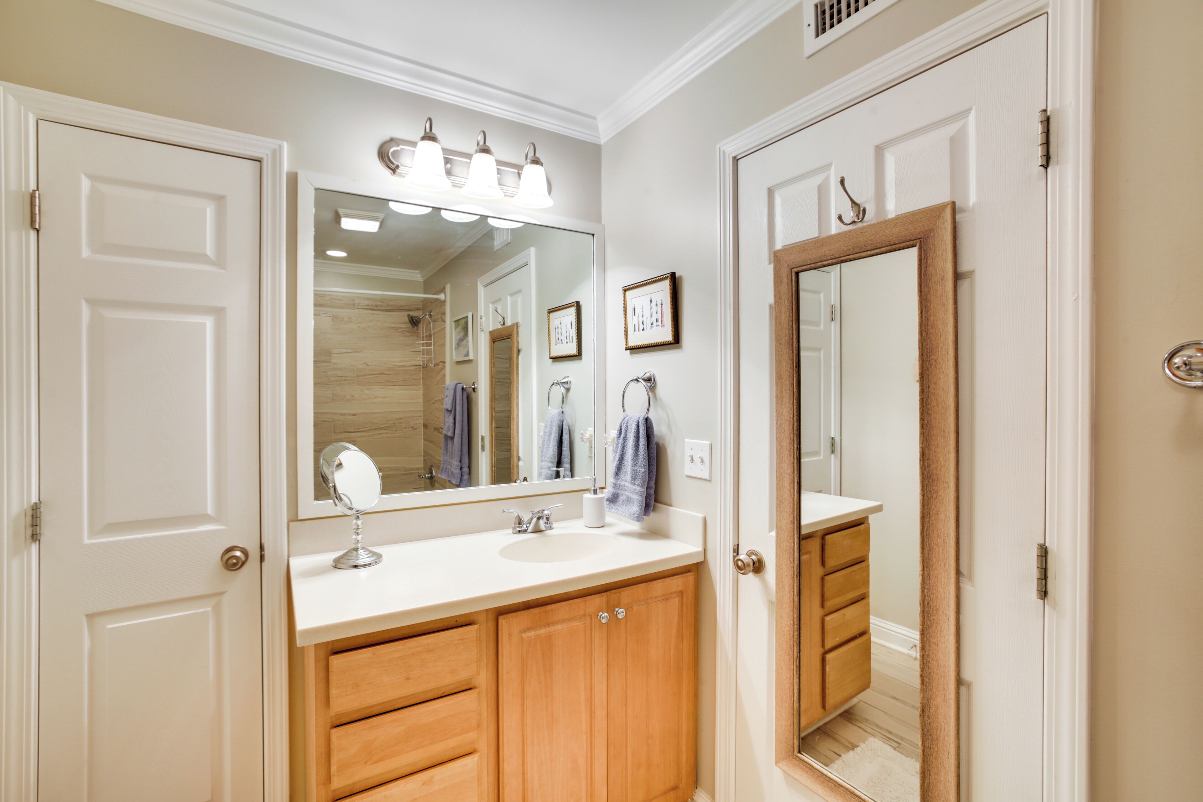 Une salle de bain avec un meuble-lavabo blanc, un grand miroir et des armoires en bois.