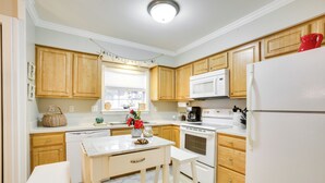 A kitchen with wooden cabinets, a white refrigerator, a stove, and a dining table with two chairs. - Old Town Bay St Louis Townhome: Walk to Beach (Bay St Louis)