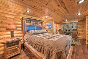 A log cabin bedroom with a wooden bed, nightstands, and a stone fireplace wall. - Dreamy Cabin Steps to Thumb Lake: Swim & Fish (Boyne Falls)
