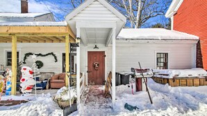 Een besneeuwde buitenruimte met een houten pergola, een wit huis met een rode gevel, en een sneeuwpop decoratie.