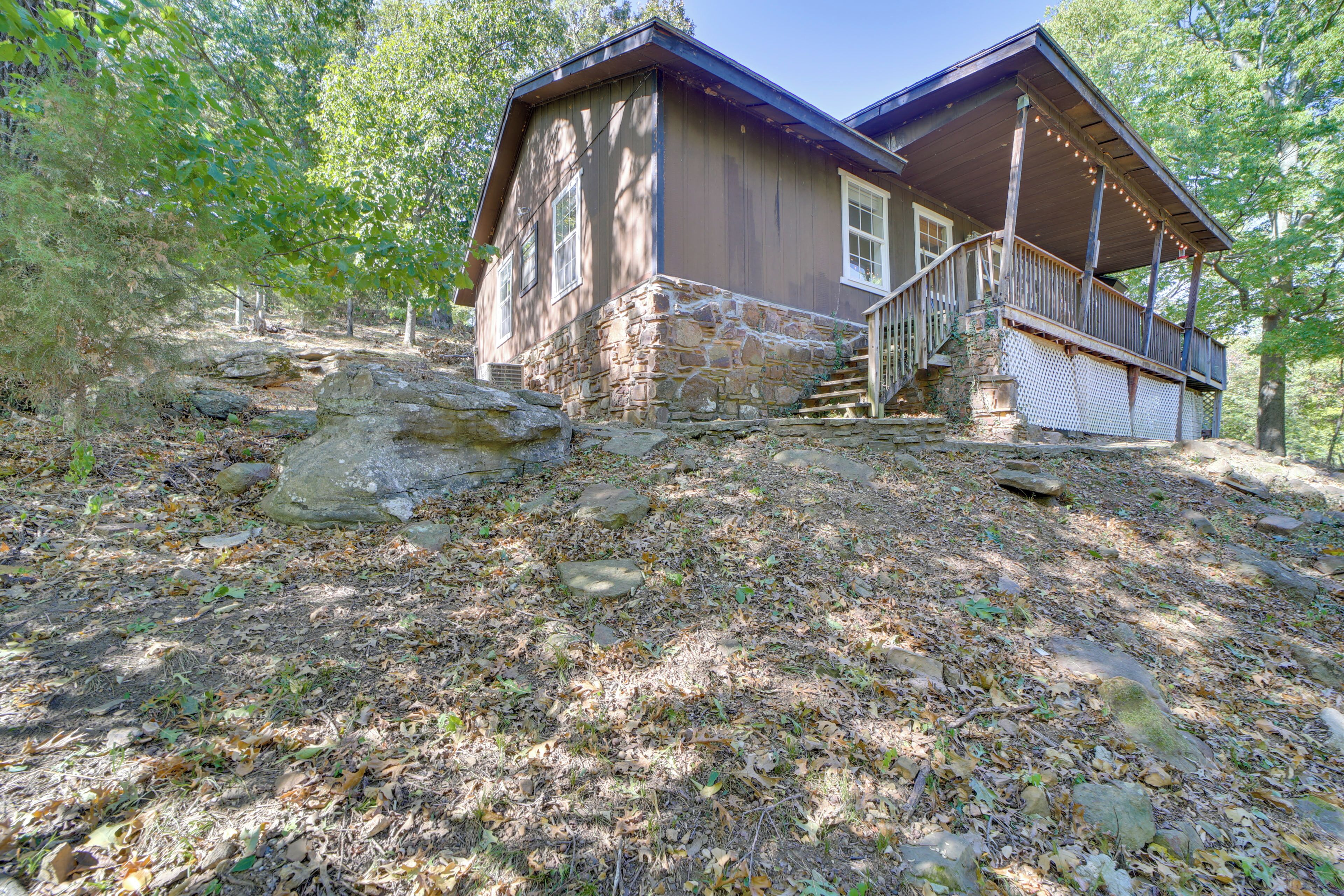 A rustic cabin with a stone foundation, wooden exterior, and a porch with string lights.