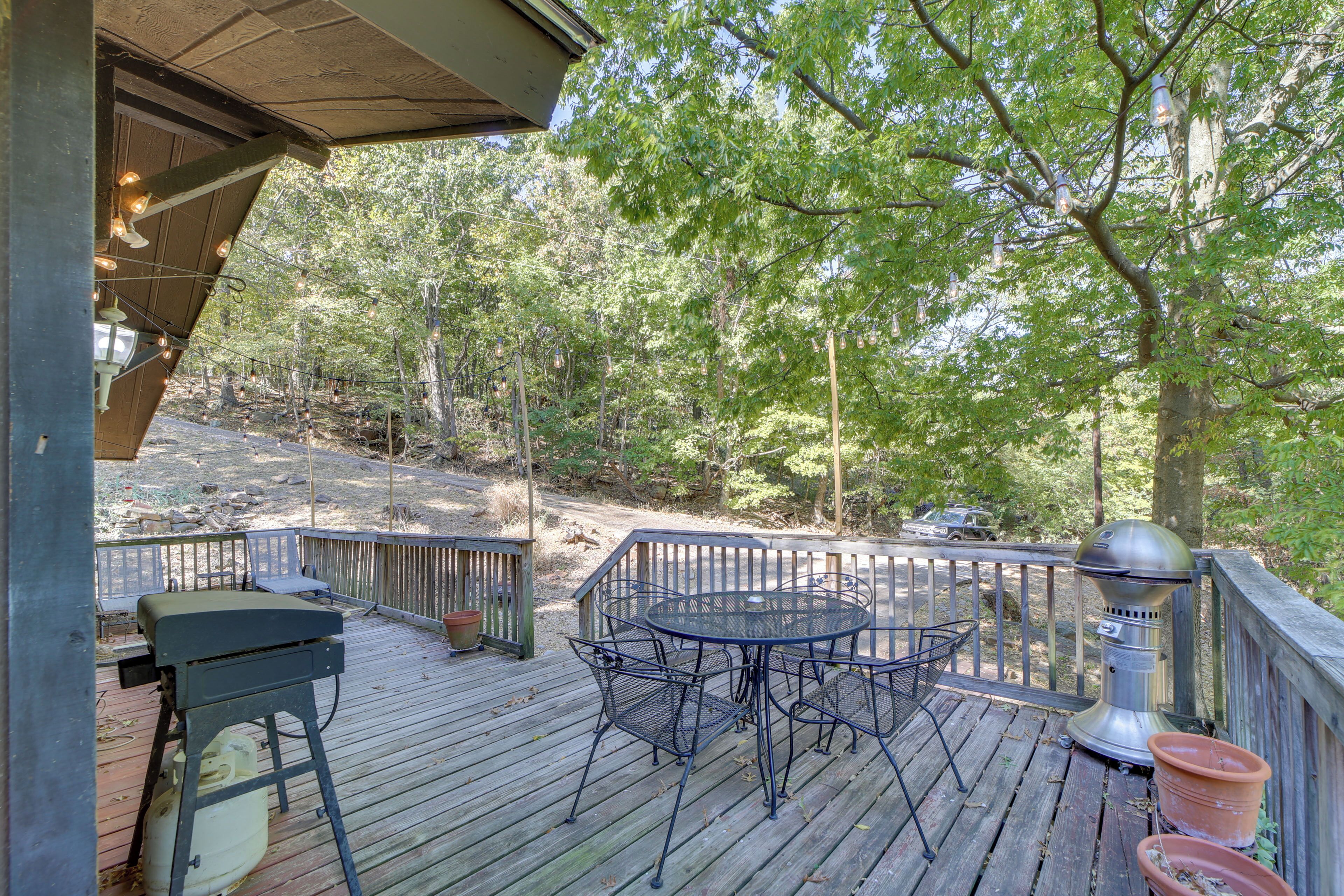 A wooden deck with a metal table and chairs, surrounded by trees.