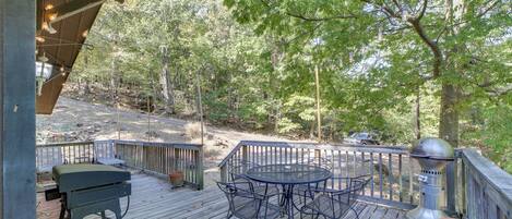 A wooden deck with a metal table and chairs, surrounded by trees.