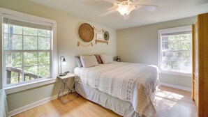 Un dormitorio con cama, dos ventanas, ventilador de techo y mesita de noche.