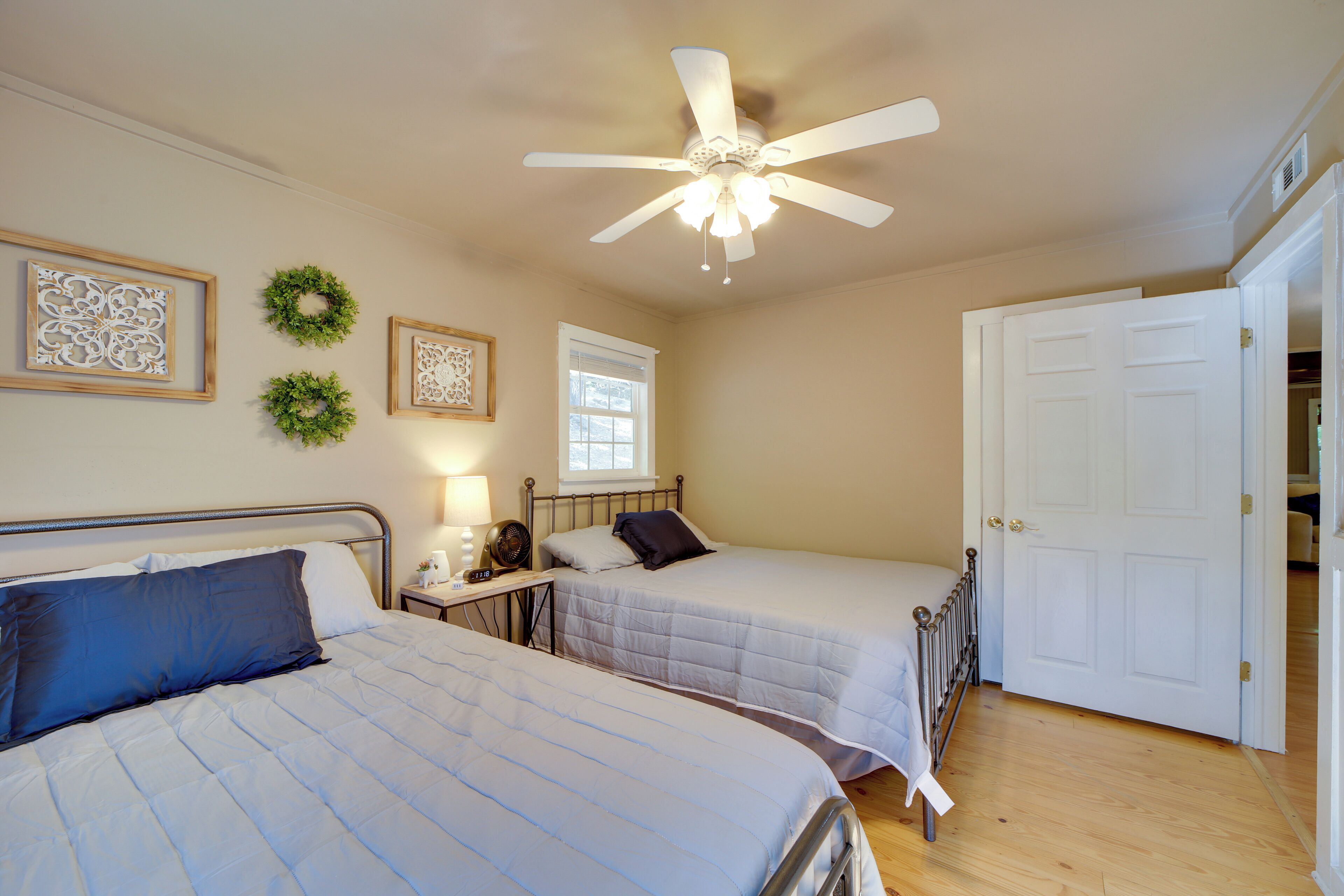 A bedroom with two beds, a ceiling fan, a window, and a door.