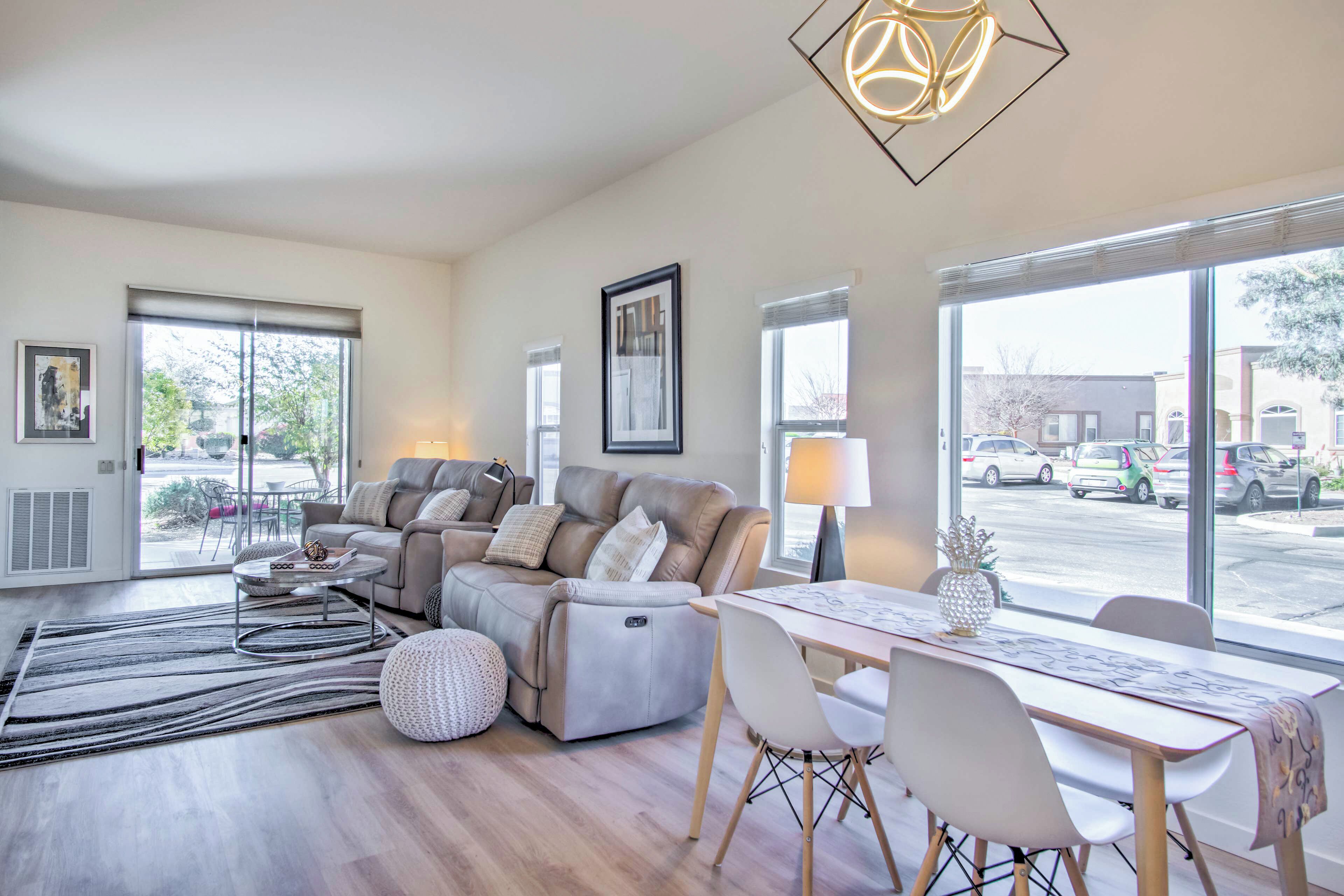 A modern living room with a sofa set, a dining table, and large windows offering a view of the street.