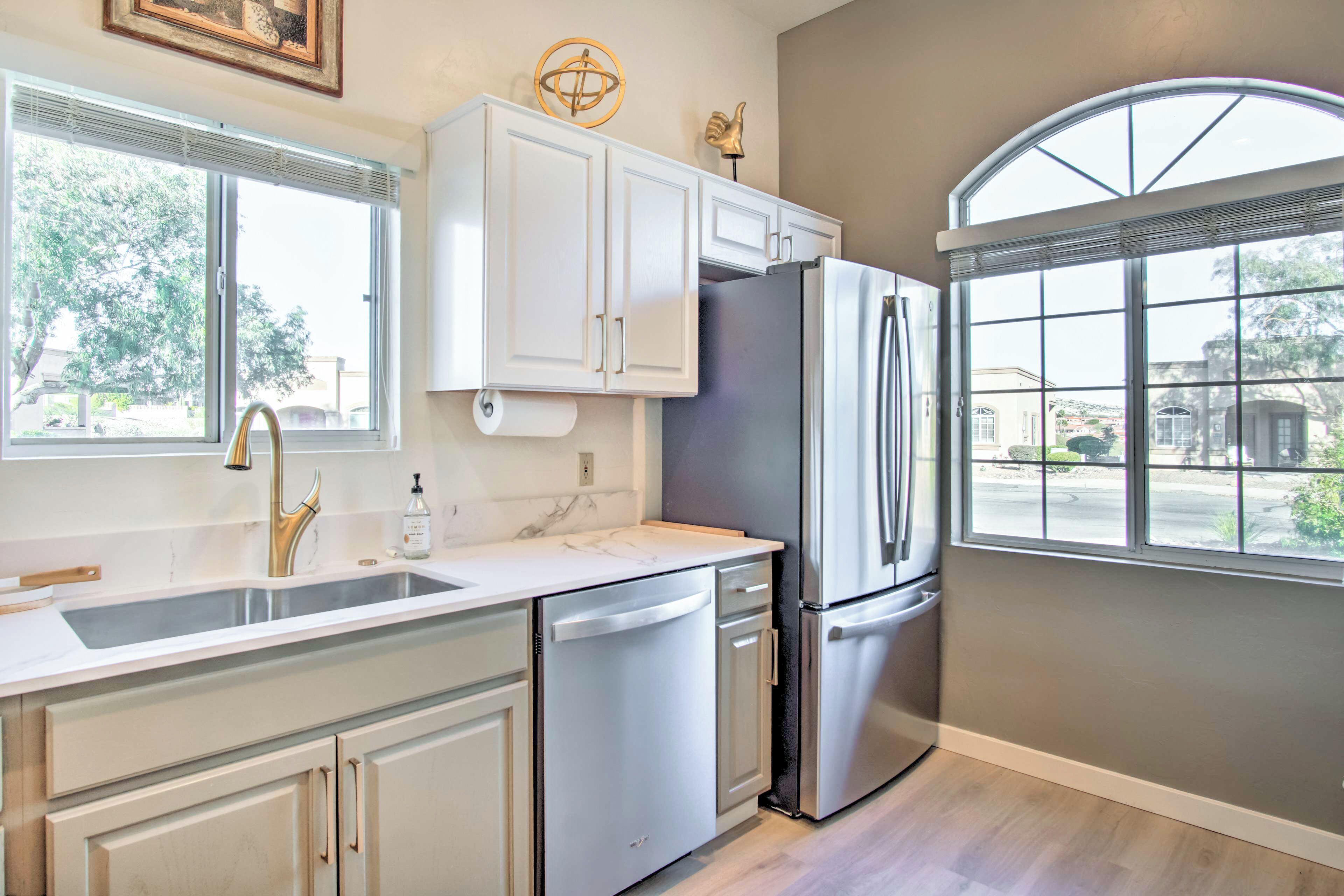 A modern kitchen with white cabinetry, stainless steel appliances, and large windows providing natural light.