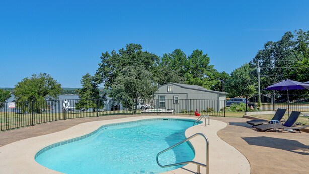 A swimming pool with a lifeguard stand, lounge chairs, and a fenced area with trees and a building in the background. - Pool & Amazing View: Updated Grand Lake Getaway (Grove)