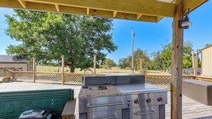 An outdoor kitchen area with a grill and a sink, under a wooden deck with a view of trees and a fence. - Pool & Amazing View: Updated Grand Lake Getaway (Grove)
