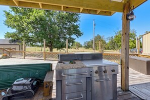 An outdoor kitchen area with a grill and a sink, under a wooden deck with a view of trees and a fence. - Pool & Amazing View: Updated Grand Lake Getaway (Grove)