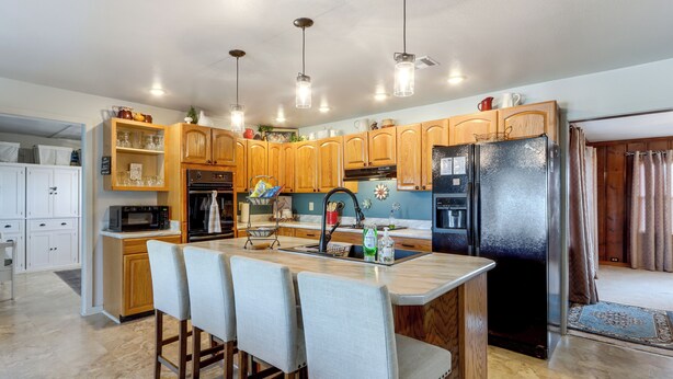 A modern kitchen with wooden cabinets, a central island with bar stools, stainless steel appliances, and pendant lighting. - Pool & Amazing View: Updated Grand Lake Getaway (Grove)