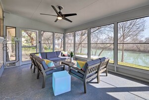 A sunroom with a ceiling fan, large windows, and a seating area with a sofa and ottoman.