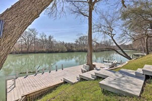 A wooden dock extending into a calm lake, surrounded by trees and grassy areas.