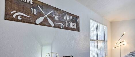 A rustic welcome sign, a hexagonal light fixture, and a framed welcome sign on a wooden table in a room with a window and a lamp.