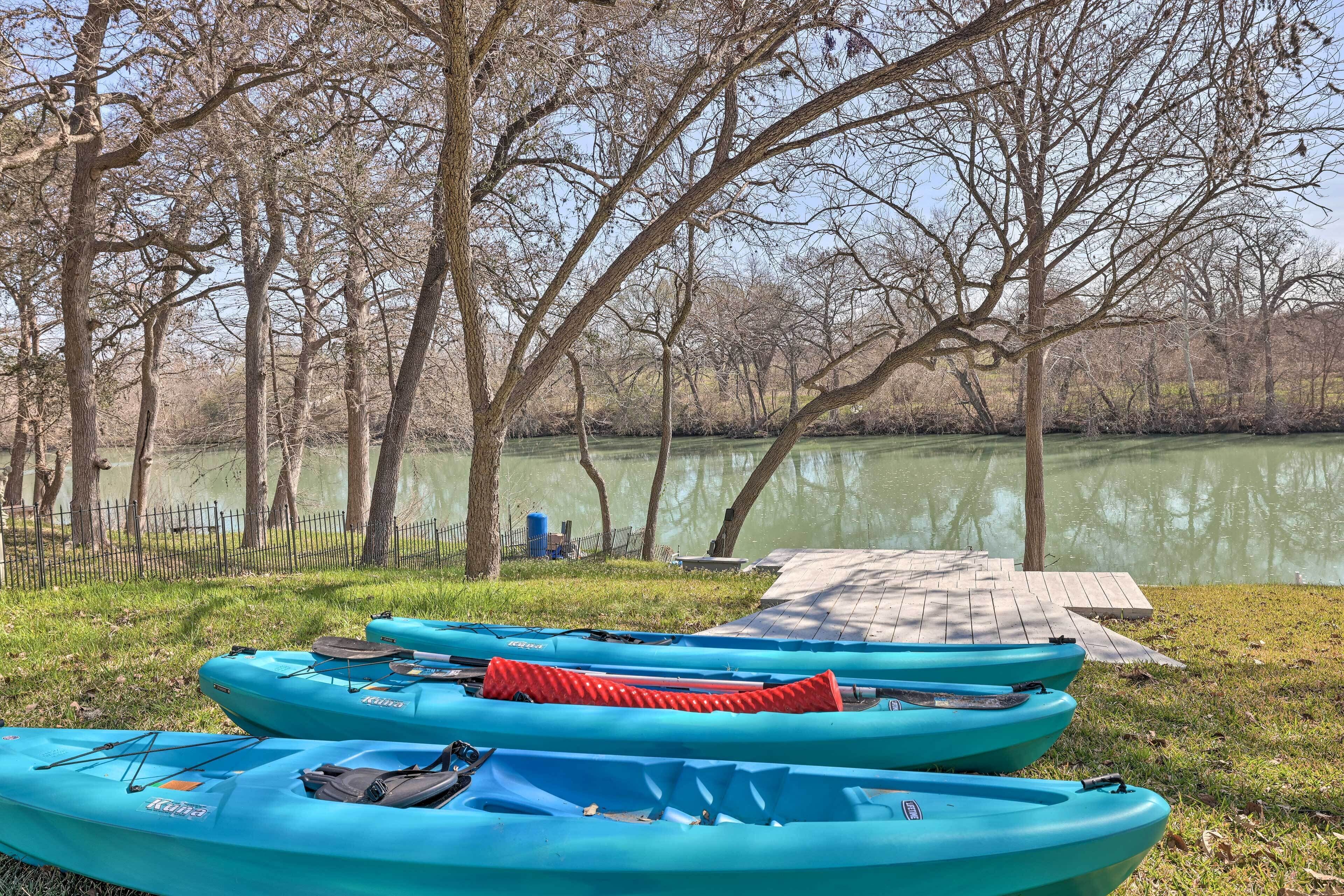 Kayaks alineados cerca de un muelle junto a un lago tranquilo, rodeado de árboles.