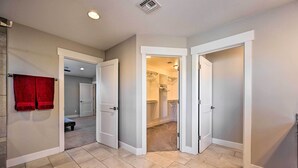 A hallway with beige tiled flooring, white walls, and a red towel hanging on the left. There are three open doors leading to different rooms. - Spacious Flagstaff Home w/ Fenced Yard & Grill! (Flagstaff)