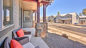 A covered outdoor seating area with wicker furniture and a stone accent. - Spacious Flagstaff Home w/ Fenced Yard & Grill! (Flagstaff)