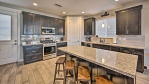 A modern kitchen with dark cabinets, granite countertops, stainless steel appliances, and a central island with bar stools. - Spacious Flagstaff Home w/ Fenced Yard & Grill! (Flagstaff)