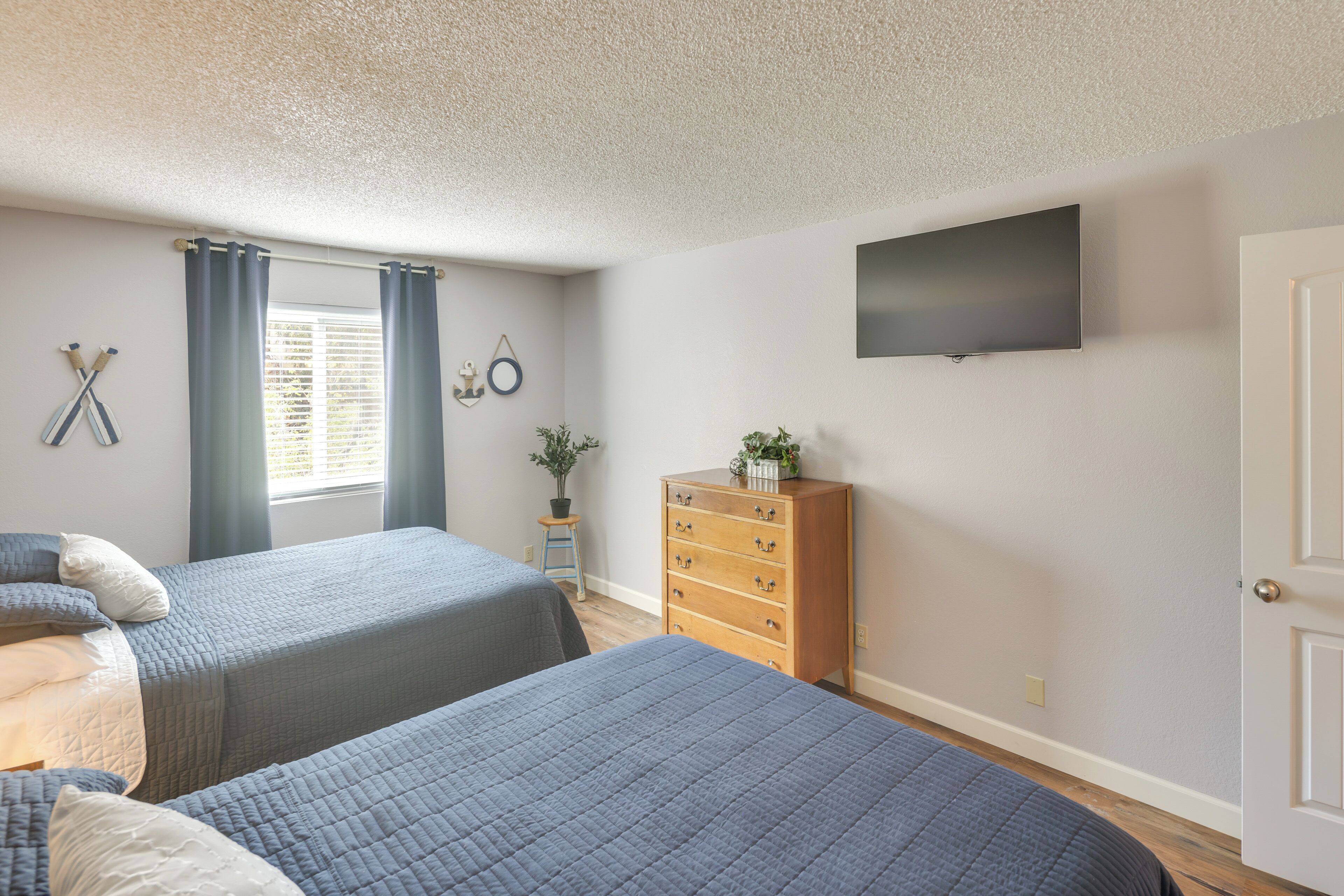 Une chambre avec deux lits, une commode, une télévision et une fenêtre avec des rideaux.