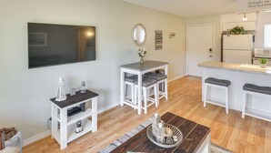 Una cocina moderna con armarios blancos, microondas empotrado y refrigerador. Hay una pequeña isla con taburetes y un espejo arriba.
