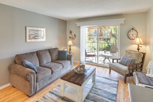 A living room with a grey sofa, a coffee table, and a chair. There is a window with a view of the outdoors.