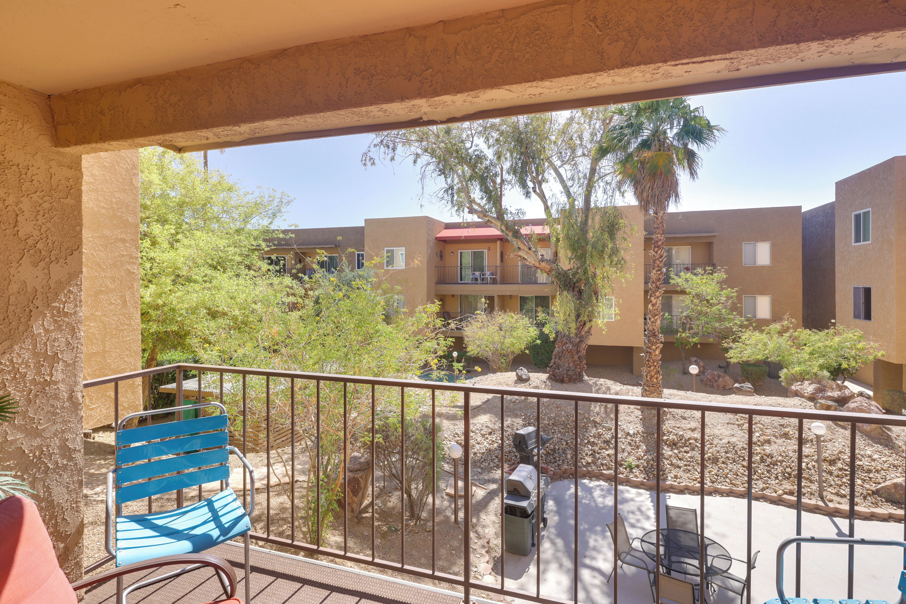 A balcony with a metal railing, a blue chair, and a table.