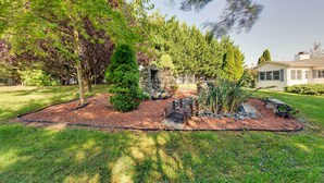 Un jardín ajardinado con un sendero de piedra, arbustos variados y una pequeña formación rocosa.