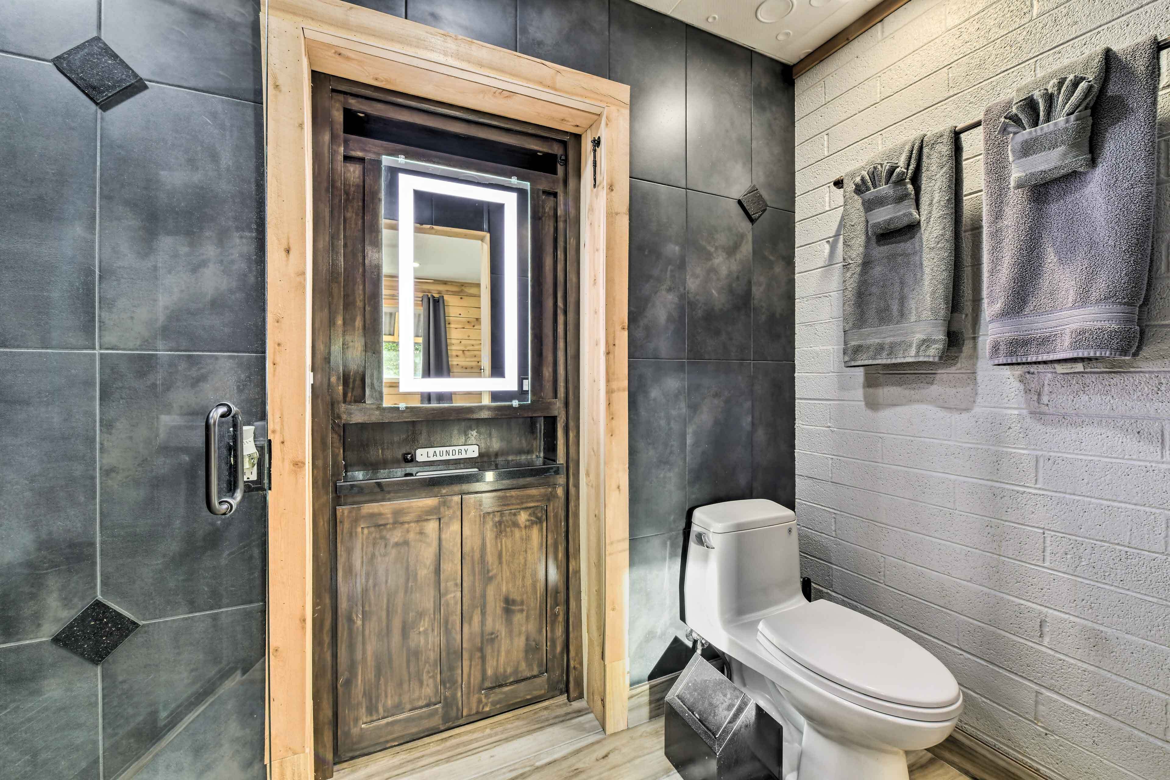 A modern bathroom with a wooden door, a visible toilet, and towels hanging on the wall.