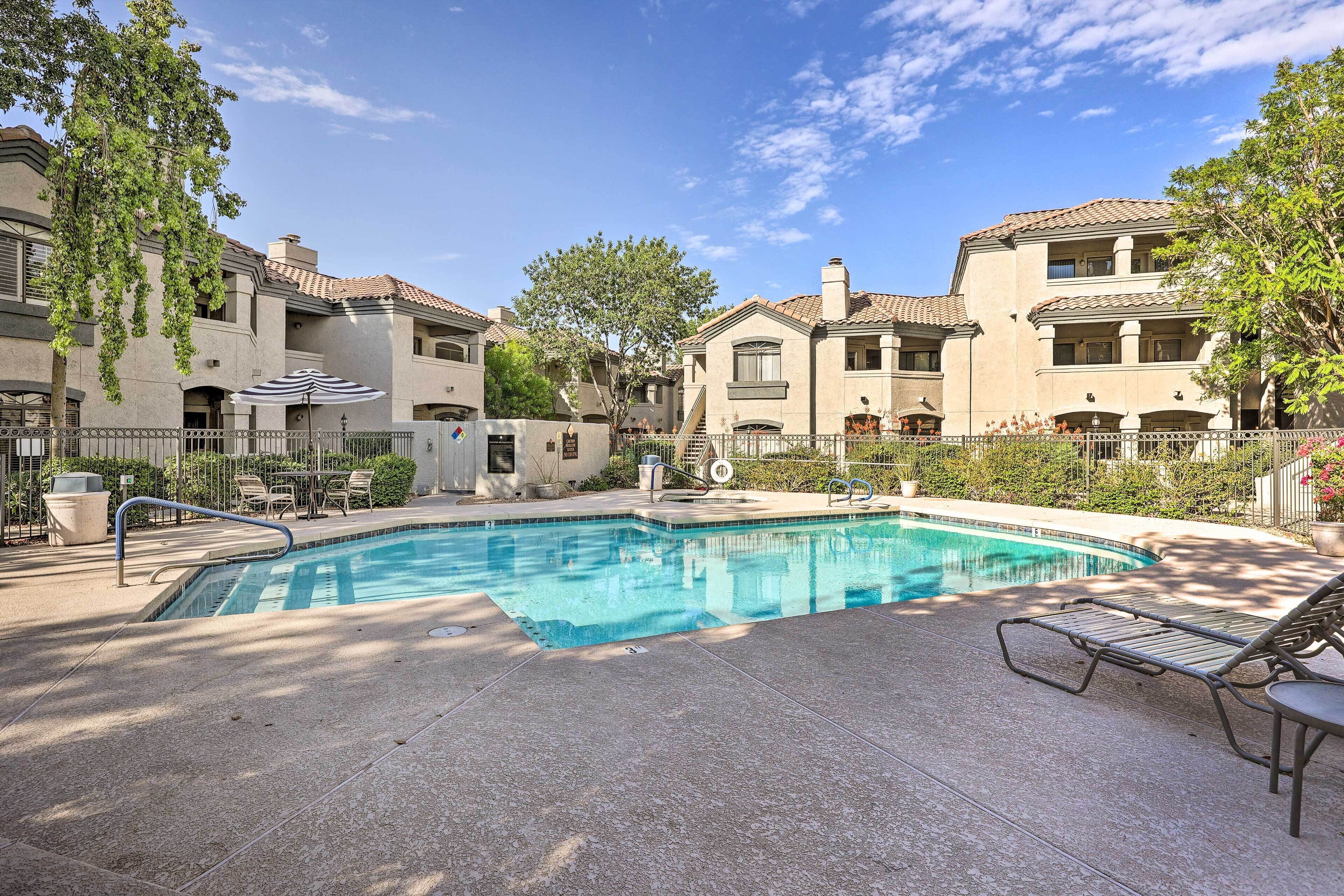 A swimming pool with lounge chairs, surrounded by multi-story buildings with balconies and trees.