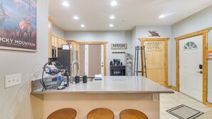 A kitchen with a central island, wooden stools, a refrigerator, and a coffee machine. - Patio & Mountain Views: Central Grand Lake Condo! (Grand Lake)
