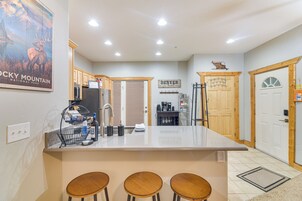 Una cocina con una isla central, taburetes de madera, un refrigerador y una cafetera.