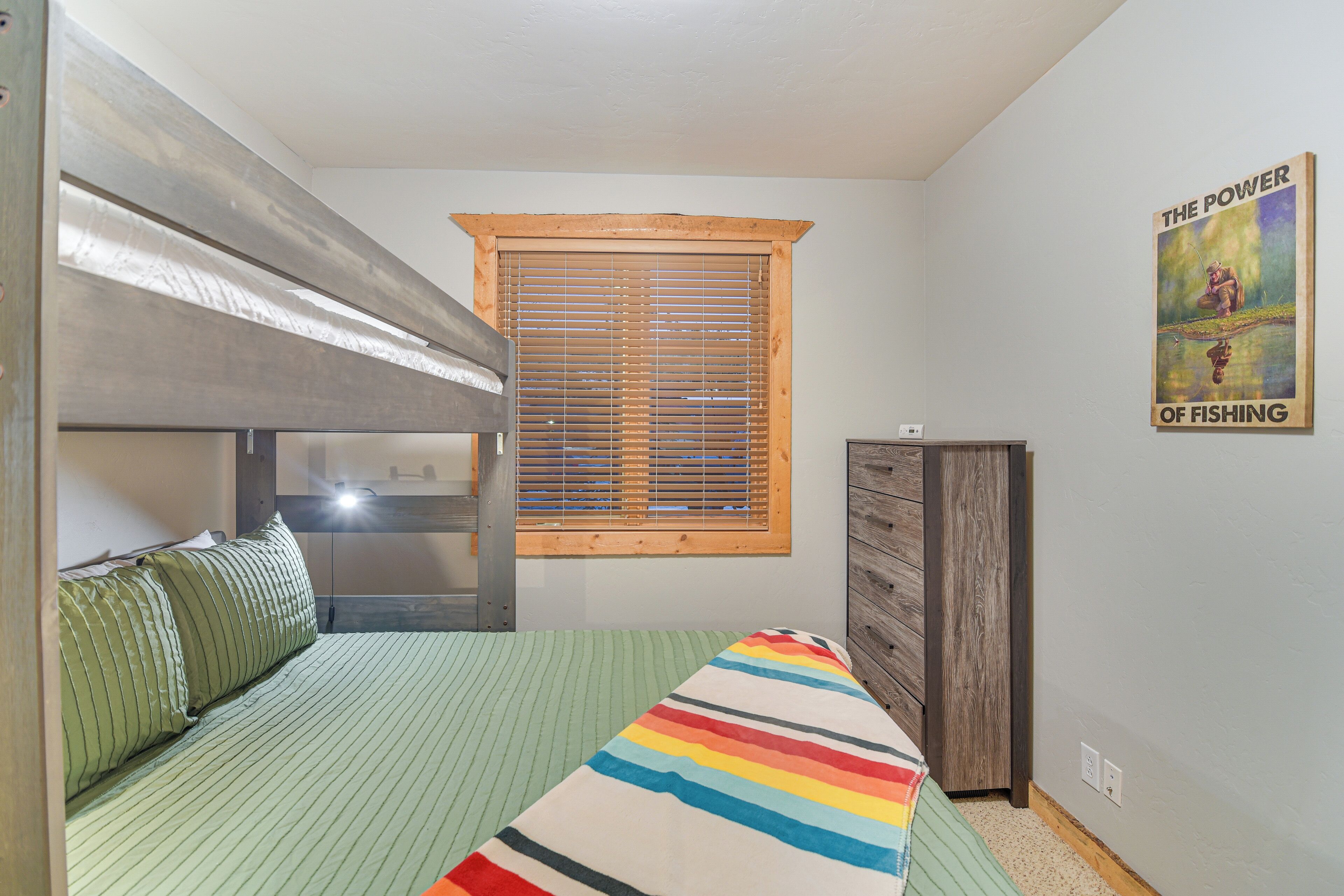 A bedroom with a bunk bed, a window with blinds, a dresser, and a poster on the wall.