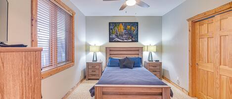 Une chambre avec un lit en bois, un ventilateur de plafond, un tableau et une armoire en bois.