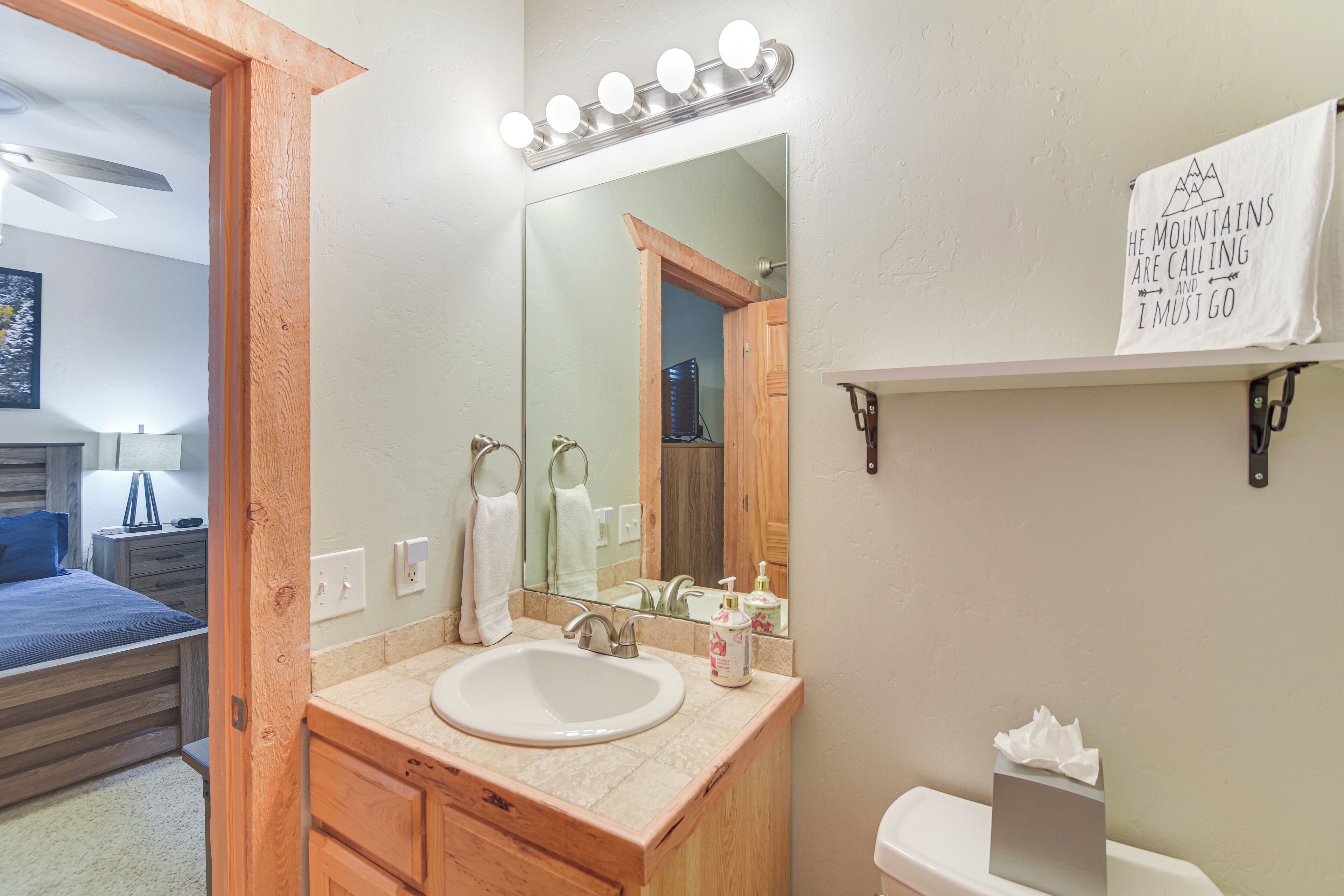 A bathroom with a wooden vanity, a sink, a mirror with lights, a towel rack, and a toilet.