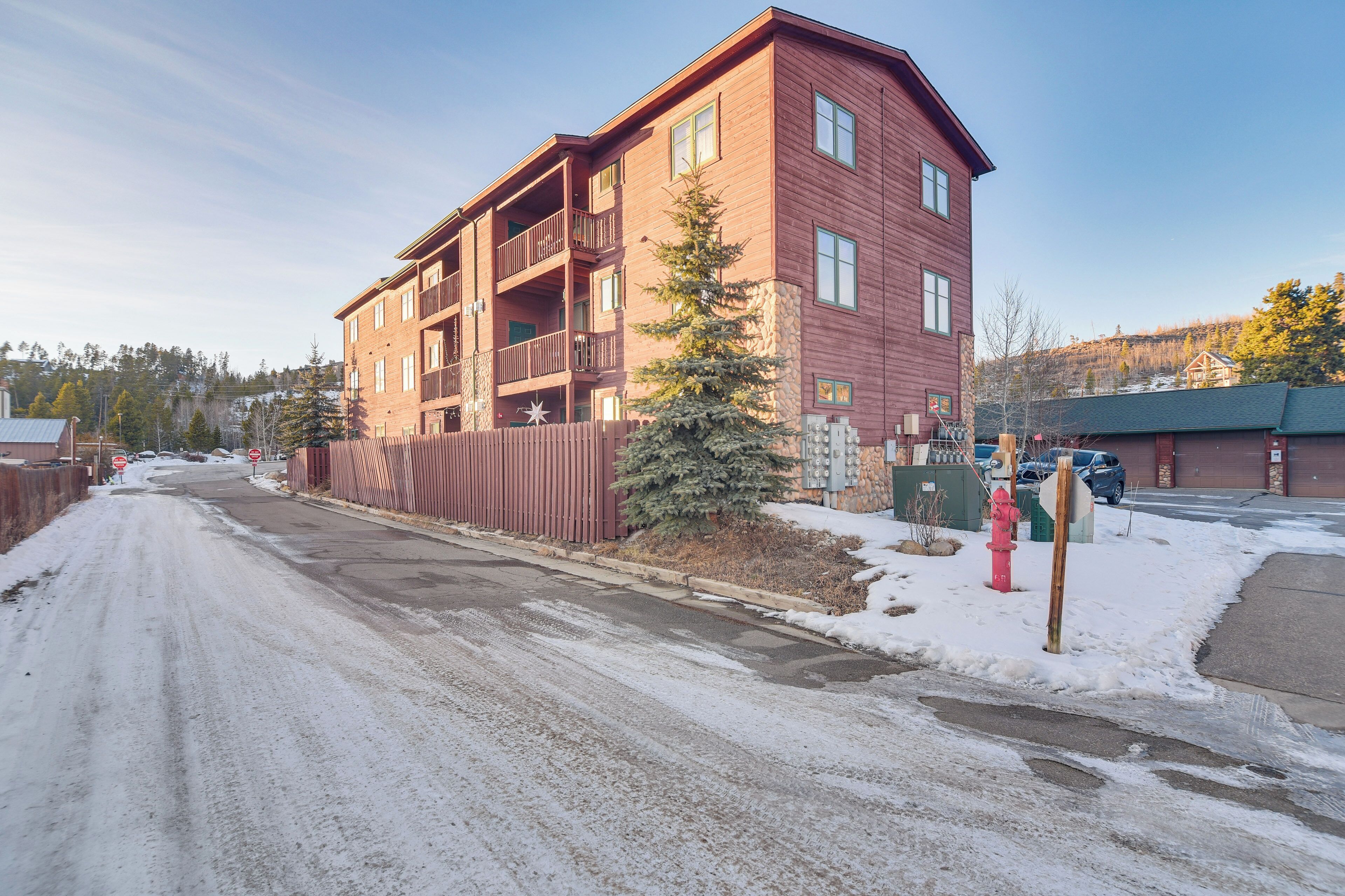 Un edificio de varios pisos con balcones, suelo cubierto de nieve y un hidrante rojo.