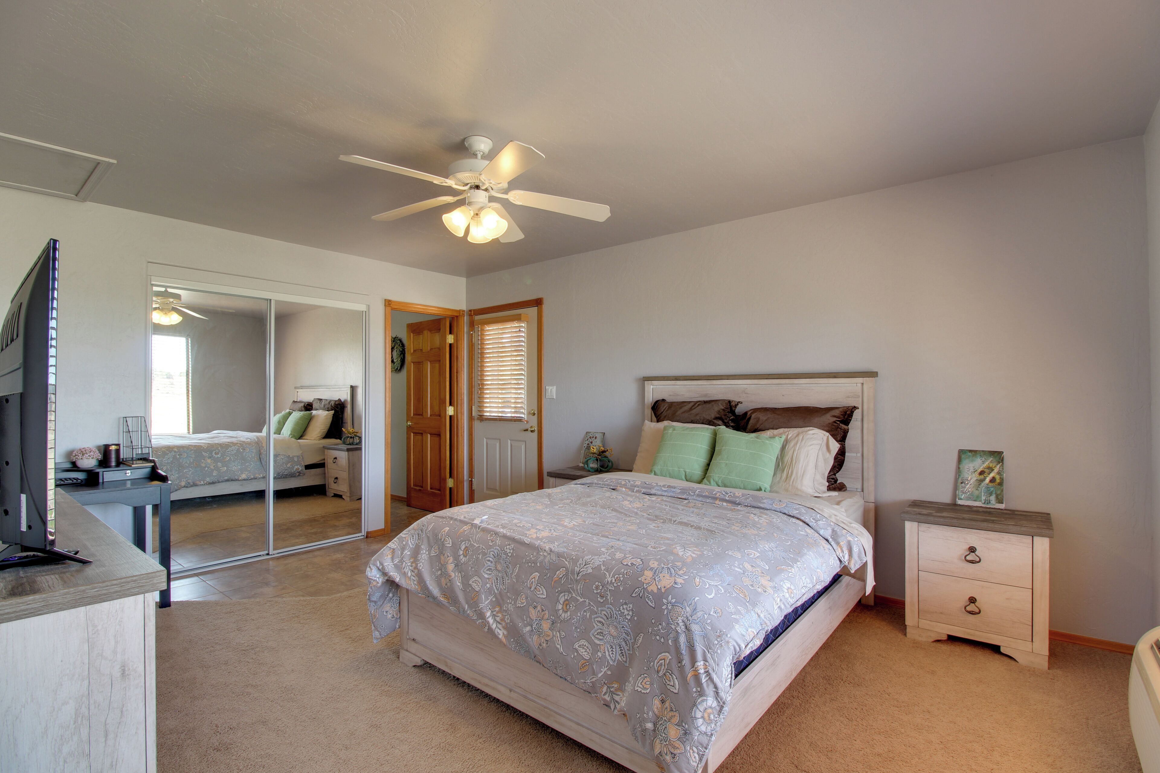 A bedroom with a bed, bedside tables, a mirror, a ceiling fan, and a TV.
