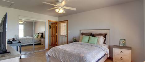 A bedroom with a bed, bedside tables, a mirror, a ceiling fan, and a TV.