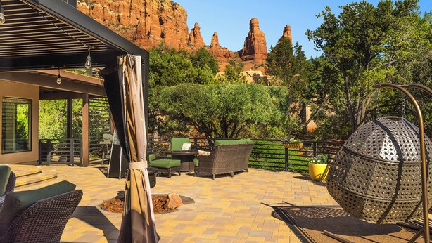 Une terrasse extérieure aménagée avec des meubles en osier, un fauteuil sphérique en métal et une vue sur des formations rocheuses rouges.
